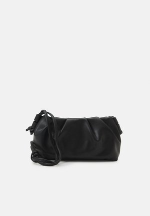 Bolso de mano de cuero negro suave con detalles fruncidos y una larga correa enrollada junto a él sobre un fondo claro y sencillo.