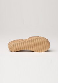 La suela de la sneaker presenta una base de goma ligera de color marrón con textura y ranuras horizontales para tracción, además de un diseño trenzado alrededor del borde.