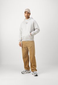 Felpa grigia con tasca a canguro, pantaloni in corduroy beige e sneakers grigie. Cappellino beige coordinato. Dettaglio del logo semplice sulla felpa.