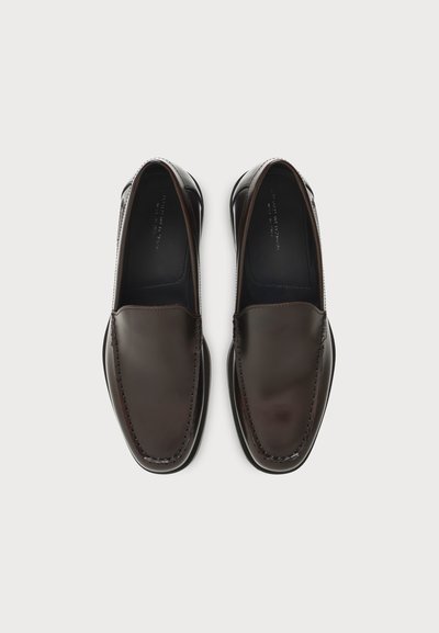 Ζευγάρι σκούρα καφέ δερμάτινα loafers χωρίς κορδόνια με στρογγυλεμένα τετράγωνα μύτη και ορατές ραφές σε λευκό φόντο.