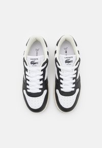 Scarpe da ginnastica in bianco e nero con tomaia in pelle liscia, punta rotonda, dettagli perforati e lacci bianchi. Logo Lacoste sulla linguetta.