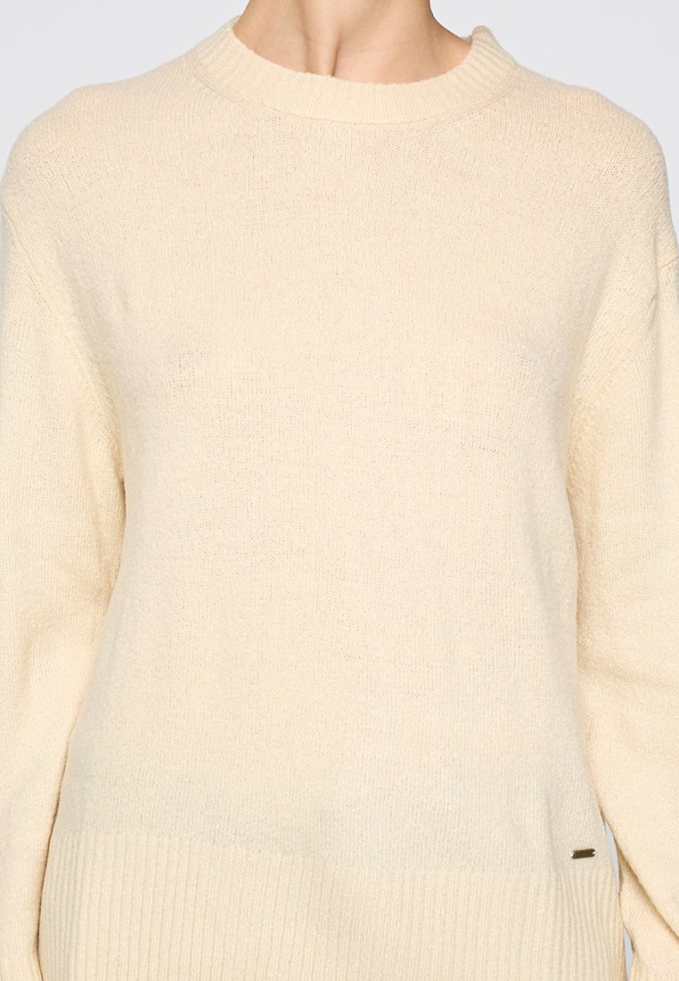 Pull en tricot crème avec un col rond, des manches longues et un ourlet côtelé. Texture douce avec de subtiles variations de teinte. Design minimaliste.