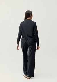 Čierny športový set obsahujúci tričko s dlhým rukávom a rozparkom na chrbte, spolu s nohavicami vo voľnom strihu. Hladká tkanina s širokými nohavicami a lemovanými koncami.