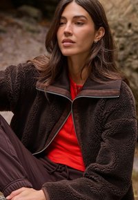 Pruun fliisist jakk lukuga kraega, kombineeritud soonikkoega punase topiga. Pehme tekstuur, vabaaja disain ja mugav lõige on silmapaistvad omadused.