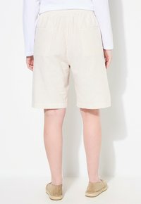 Bežové pruhované šortky s elastickým pasem, dvěma zadními kapsami a délku ke kolenům, doplněné o bežové espadrilky.