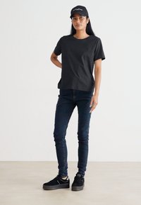 Black cotton t-shirt with a crew neck, paired with dark skinny jeans. Black sneakers with a thick sole. A black cap completes the outfit.