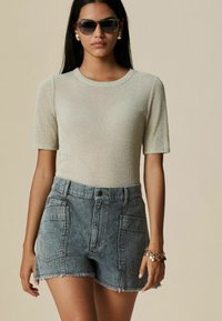 Käivalt helkiv heledalt roheliselt lühikeste varrukatega pluus ümarate kaelustega, kombineeritud kõrge vöökohaga kulunud denim lühikesed püksid, millel on ees taskud.