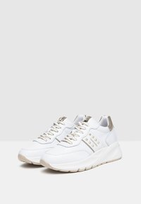 Scarpe da ginnastica bianche con una superficie in pelle liscia, accenti metallici dorati, suole testurizzate e borchie decorative sul lato.