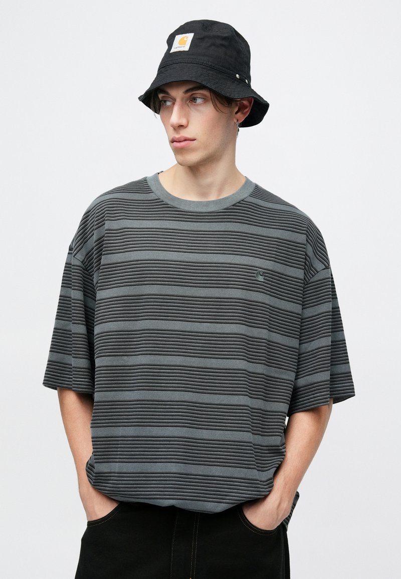 Gray striped t-shirt with horizontal ridges and a crew neckline, paired with a black bucket hat featuring a branded logo patch.