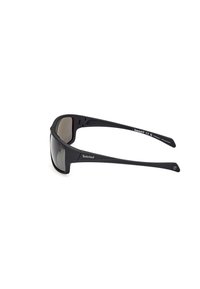 Gafas de sol de plástico negro con lentes grises, diseño envolvente y marca Timberland en la patilla. Textura suave y forma elegante.