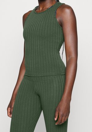 Ærmeløs, ribbet mørkegrøn tætsiddende top og matchende højtaljede ribbede bukser båret af en person med mørk hud.