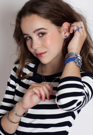 Gestreept marineblauw en witte shirt, zilveren sieraden, blauwe armband en horloge. Oorbellen in de vorm van een hart. Warme huidtinten en natuurlijke make-up.