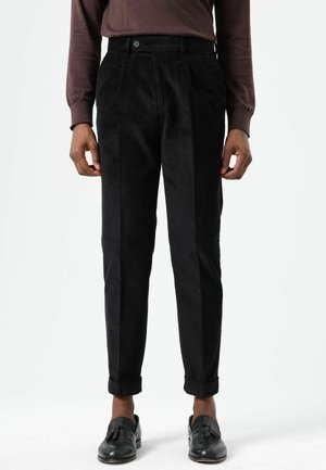 Zwarte corduroy broek met taps toelopende pasvorm, voorzien van voorplooien en zijzakken, omgeslagen boorden en een gladde textuur.