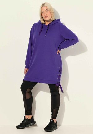 Lila Kapuzen-Tunika mit einer Kordelzugkapuze, seitlichen Schnürdetails und einer lockeren Passform, kombiniert mit schwarzen Leggings mit Netzdetails.