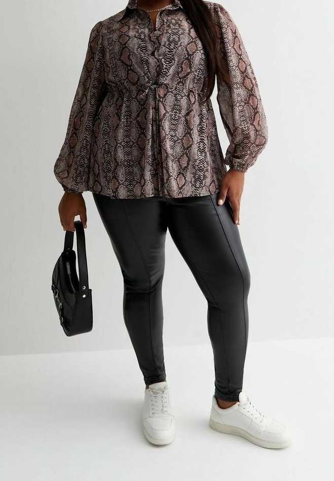 Femme portant un chemisier à manches longues à imprimé peau de serpent, des leggings noirs en simili cuir, des baskets blanches et tenant un sac à main noir à côté d'elle.