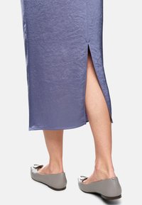 Hellpurpurener Leinenrock mit seitlichem Schlitz und glatter Struktur, kombiniert mit grauen Ballerinas mit dekorativen Schleifen.