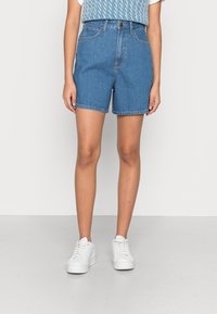 Vaaleansiniset denimshortsit, korkeavyötäröiset, viidellä taskulla, vyölenkeillä ja rispaantuneella helmalla. Yhdistetty valkoisiin tennareihin ja neulepaitaan.