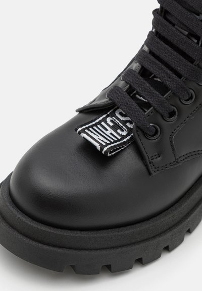 Botte de combat en cuir noir avec une semelle épaisse et texturée. Présente des lacets noirs et une étiquette de logo sur la languette. Design à bout arrondi.