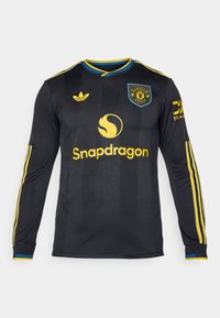 Black long-sleeve football jersey with yellow accents. Features snapdragon logo and club crest. Striped shoulders and textured fabric.