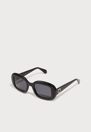 Gafas de sol rectangulares negras con lentes oscuros, montura gruesa y brillante, y acento de logo circular en tono dorado en las patillas.