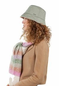 Gestepptes grünes Bucket Hat mit breiter Krempe und dezenten Stickdetails; getragen mit einem gestreiften, mehrfarbigen Wollschal.