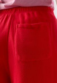 Punased pehmed riidest püksid elastse vöökohaga ja ühe ümmarguse tagataskuga, kantud heledaroosa topiga.