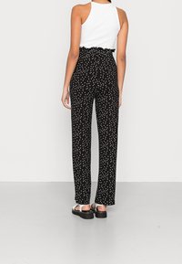 Pantalons noirs à pois avec une taille haute froncée, coupe ample et tissu léger. Assortis à des sandales plates en argent.