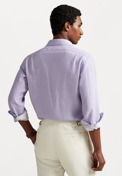 Chemise lilas clair avec un petit motif, manches longues retroussées, ourlet arrondi et col pointe, associée à un pantalon couleur crème.