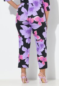 Hosen mit Blumenmuster, großen lila und rosa Blüten auf schwarzem Hintergrund, konisch zulaufende Beine und ein selbstbewusster Schnitt. Kombiniert mit pinken High Heels.