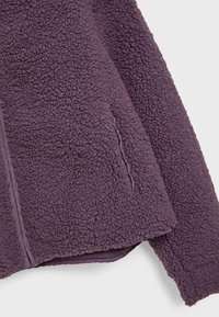 Giacca in pile viola con una superficie esterna texturizzata e un rivestimento interno liscio, dotata di una tasca laterale e dettagli di cucitura a contrasto.