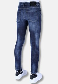 Donkerblauwe skinny jeans van denim, met een vervaagde textuur, achterzakken en een zwarte taillebandlabel. Gecombineerd met witte sneakers.