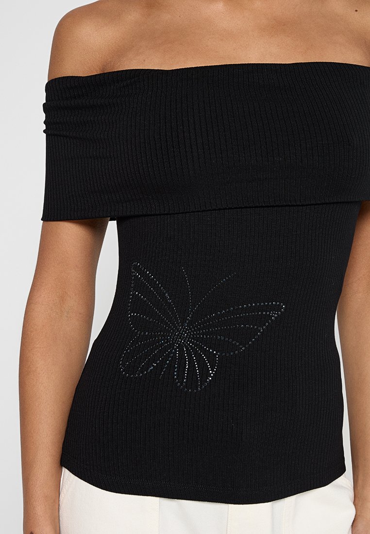 Haut noir en maille côtelée décolleté épaule dénudée avec un design de papillon en rhinestones au niveau de la taille, en tissu près du corps et texturé.