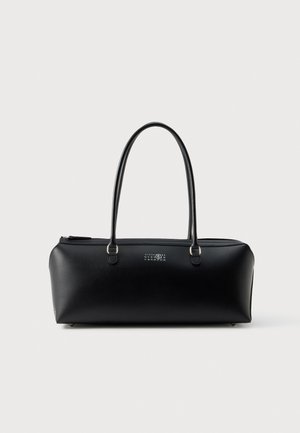 Sac à main noir en cuir structuré, doté de deux longues anses, d’une fermeture éclair sur le dessus et d’un petit logo blanc numéroté, sur un fond uni.