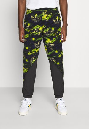 Trainingshosen mit einem grün-schwarzen abstrakten Muster und Adidas-Logo, kontrastierenden schwarzen Einsätzen und elastischen Bündchen.