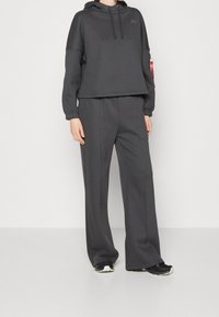 Ciemnoszara bluza z kapturem i elastycznymi mankietami, zestawiona z pasującymi szerokimi spodniami. Miękka tekstura, minimalne oznakowanie na bluzie.