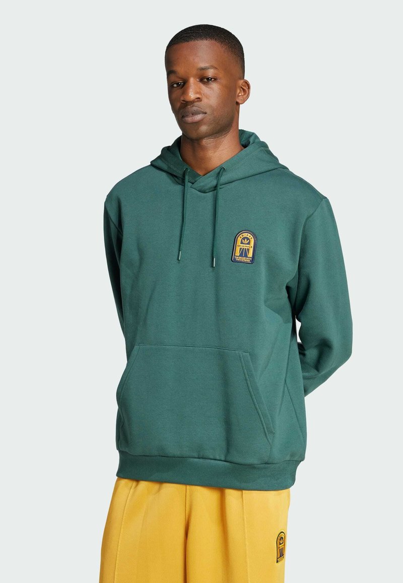 Felpa verde con cappuccio regolabile, tasca frontale e logo ricamato. Realizzata in tessuto morbido; vestibilità rilassata. Abbinata a pantaloni gialli.