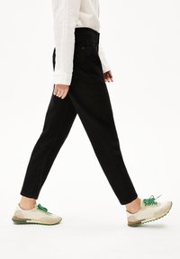 Svarta raka jeans i kombination med beige och gröna sneakers; skorna har rund tå och texturerade detaljer. Vit långärmad skjorta.