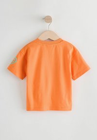 Oranža īsām piedurknēm T-kreklu, izgatavots no kokvilnas. Tam ir apaļa kakla izgriezums un tirkīza krāsas logotipa elements kreisajā piedurknē.