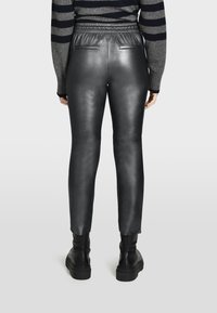 Zwarte leren leggings met een elastische tailleband, slim fit, achterzakken en zichtbare naden, gecombineerd met zwarte enkellaarzen.