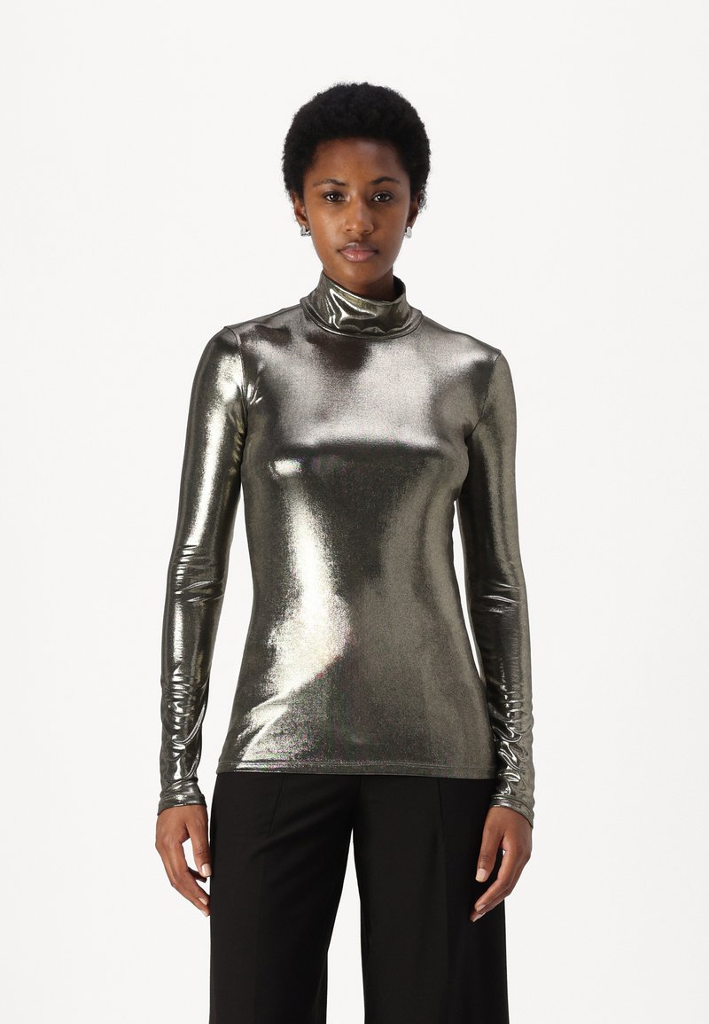 Metallicinė sidabrinė ilgomis rankovėmis aukštu kaklu palaidinė, pasižyminti elegantišku, prigludusiu siluetu ir lygiu paviršiumi, derinama su juodomis plačiomis kelnėmis.