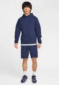 Granatowa bluza z kapturem i dopasowane spodenki z miękkiego materiału. Bluza ma sznurek ściągający i małe logo, spodenki mają elastyczny pas.