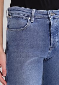 Bleknade blå denimjeans med en åtsittande design, som har fem fickor, kopparbeslag och sömnadsdetaljer längs sömmarna.