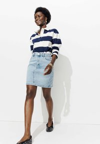 Polo à manches longues rayé bleu marine et blanc associé à une jupe en denim bleu clair. Les accessoires incluent des bracelets et des chaussures noires à pois.