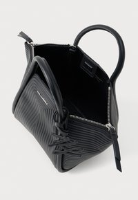 Svart quiltet skinnveske med runde håndtak, åpen glidelåsåpning, og dekorativ logo charm festet nær håndtaket.