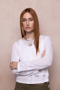 Top alb cu mânecă lungă, dintr-un material texturat cu striații, având un croi scurt și un design stratificat, asortat cu pantaloni de culoare verde măsliniu și bijuterii argintii.