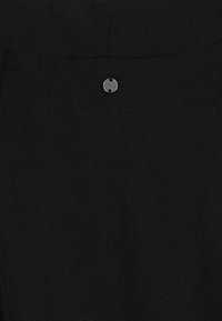 Close-up of black fabric with a small round silver metal button engraved with "SBLV CNOMP" stitched near the top center.