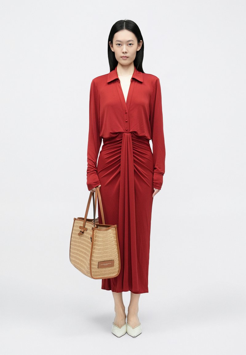 Κόκκινο φόρεμα με μακριά μανίκια, με πλαίσιο με κουμπιά και ρυτιδωτό σχέδιο. Συνδυασμένο με πλεκτή μπεζ τσάντα ώμου και μυτερά λευκά τακούνια.