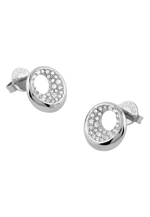 Boucles d'oreilles puces rondes en argent avec un centre creux, incrustées de petits cristaux clairs, portant le nom de la marque Guess sur la tige.