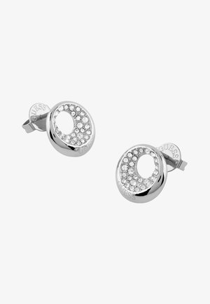 Boucles d'oreilles puces rondes en argent avec un centre creux, incrustées de petits cristaux clairs, portant le nom de la marque Guess sur la tige.