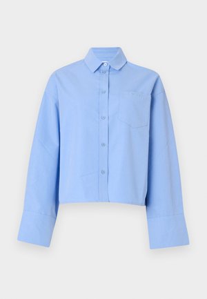 Lichtblauwe cropped shirt van stof, met een knoopsluiting aan de voorkant, grote manchetten en een borstzak met subtiele branding.